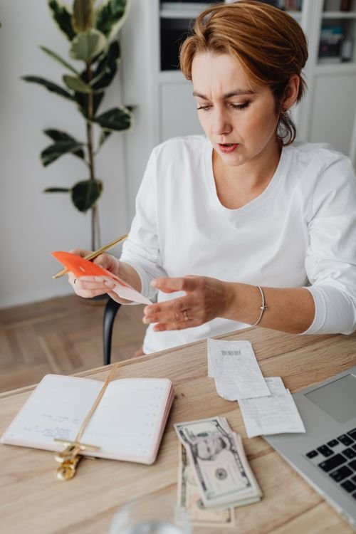 Woman calculating monthly expenses with a calculator and notebook at home, surrounded by receipts and cash